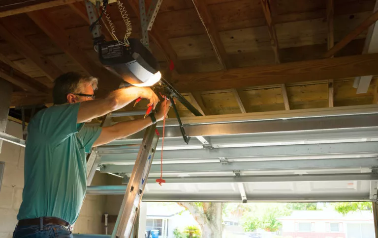 Technician standing on a ladder, repairing a garage door opener