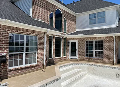 ack of a large brick home with different window styles, including double-hung with grids, picture windows and round-top windows.