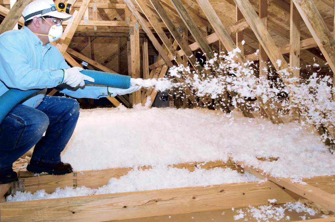 Technician installing blown-in loose-fill fiberglass insulation in an unfinished attic.