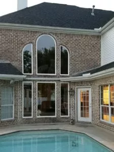 Completed replacement of large round-top windows on brick home with pool in foreground.