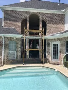 Replacement of large, round-top windows on brick home with pool in foreground. Scaffolding in front of window before replacement is complete.